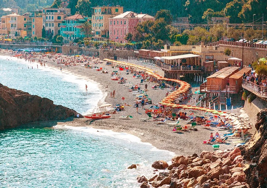 Cinque Terra beach, where rows of bright umbrellas and loungers form a lively patchwork against the soft gray sand.