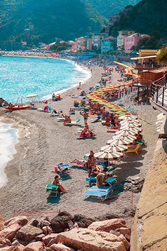 Summer beach scene in Cinque Terra seaside village with colourful rows of umbrellas and blue sea