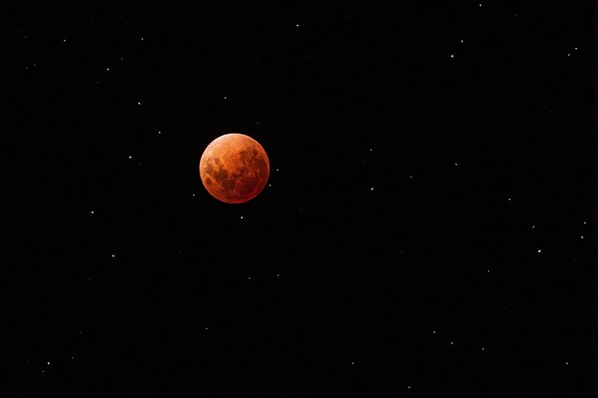 Red blood moon during lunar eclipse surrounded by stars in night sky.