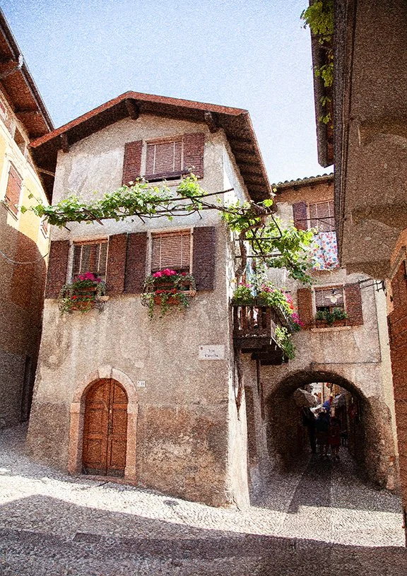 Historic European village street with rustic stone buildings, shutters and archway passage.