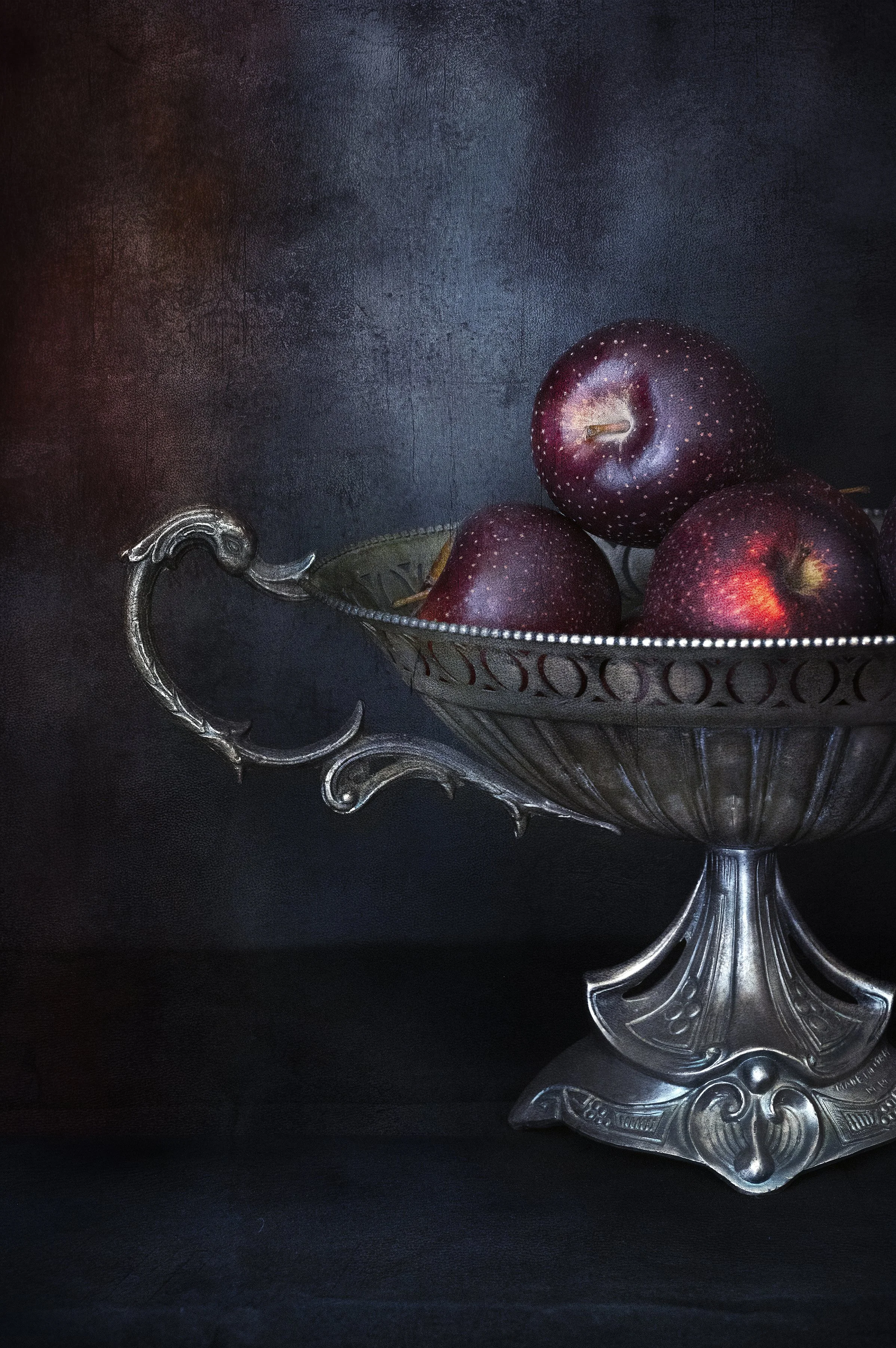 Red apples in antique silver bowl in moody still life photography.
