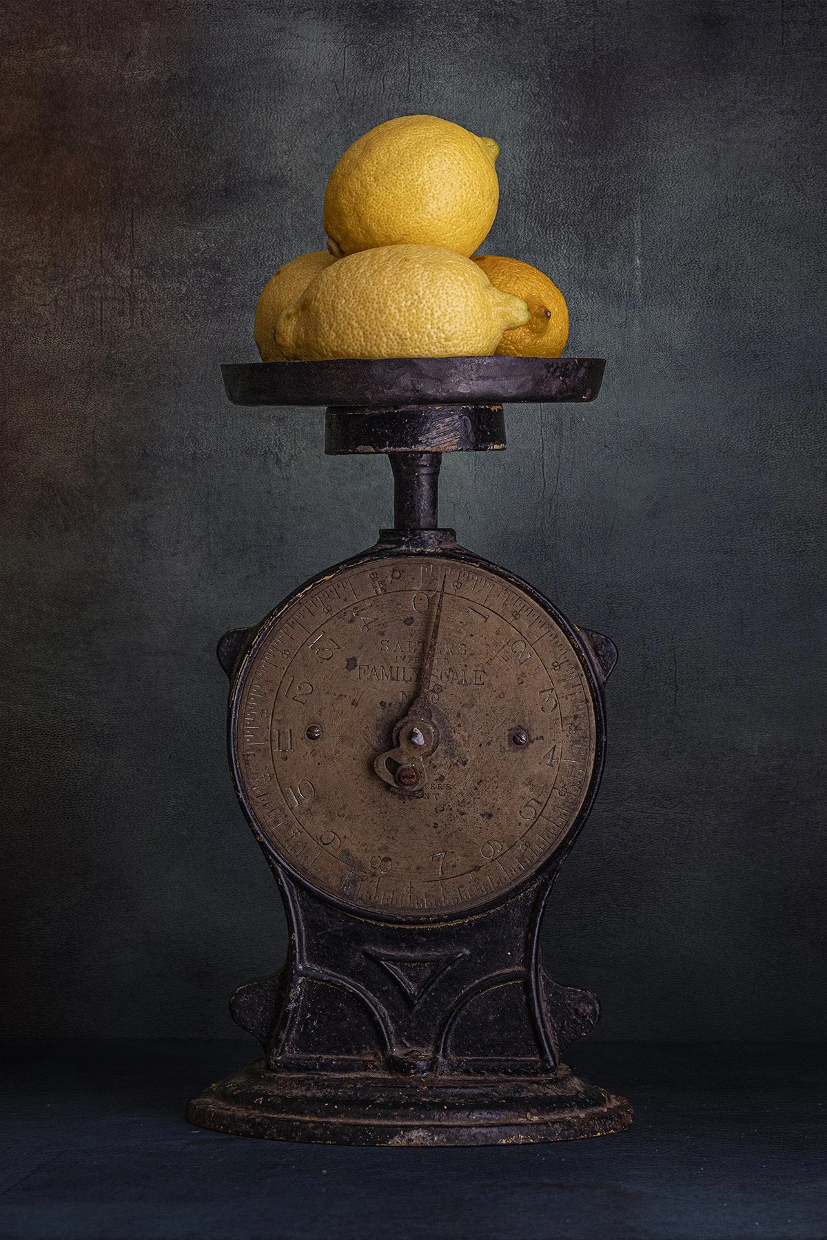 Yellow lemons stacked on a vintage kitchen scale against a textured background.