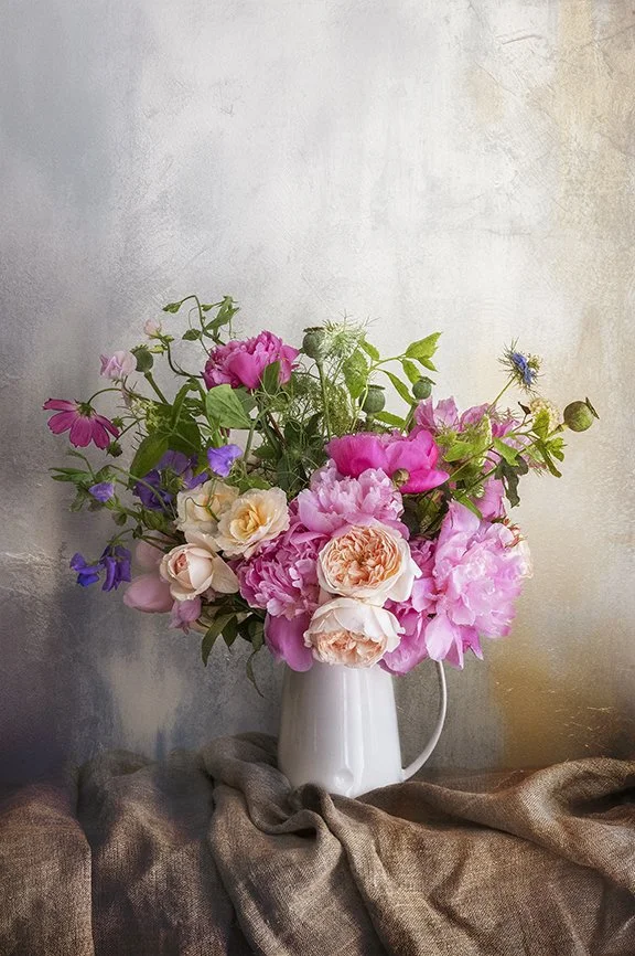 Garden bouquet of peonies and roses arranged in a white jug.
