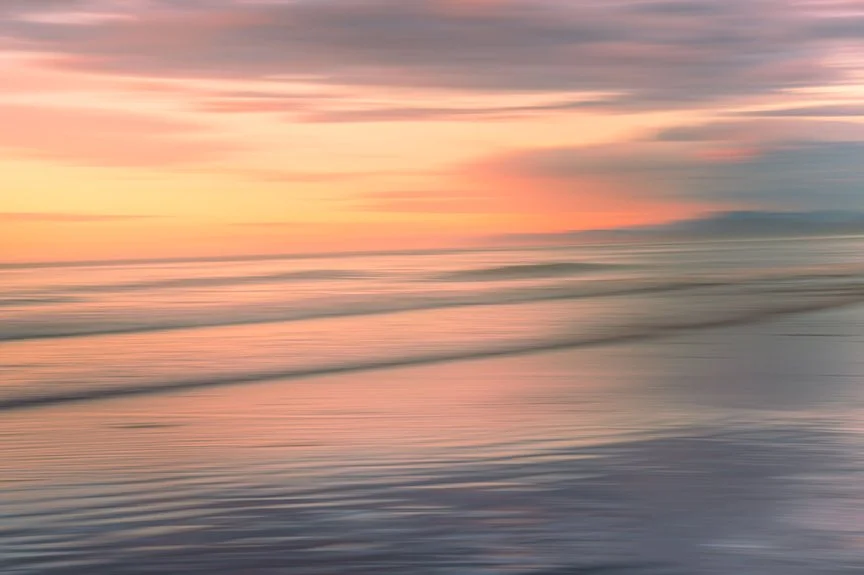 Soft blurred ocean waves at sunset with pink and peach tones.