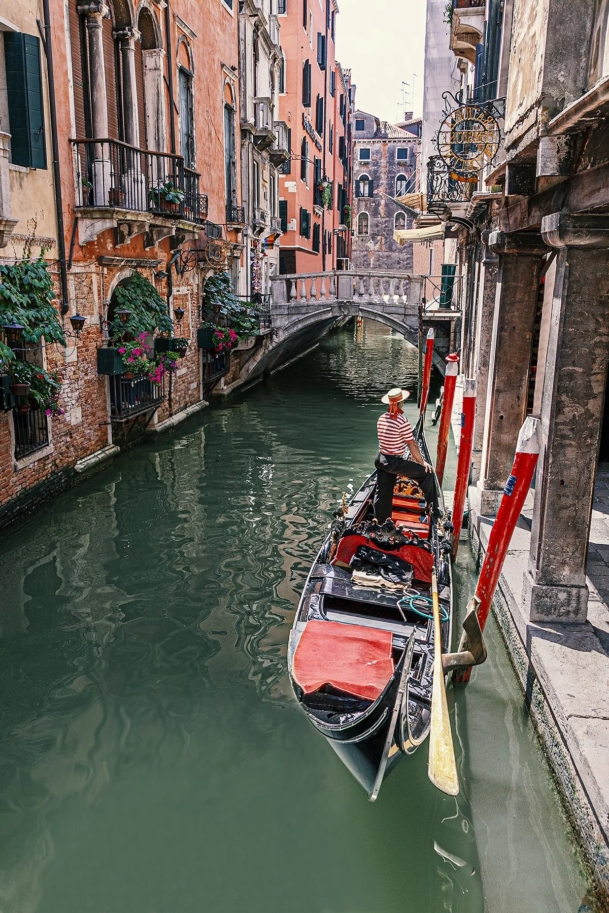 Gondolier navigating a narrow canal in Venice surrounded by historic buildings.