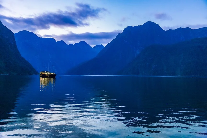 Boat anchored on calm water at blue hour in Milford Sound Fiordland New Zealand.