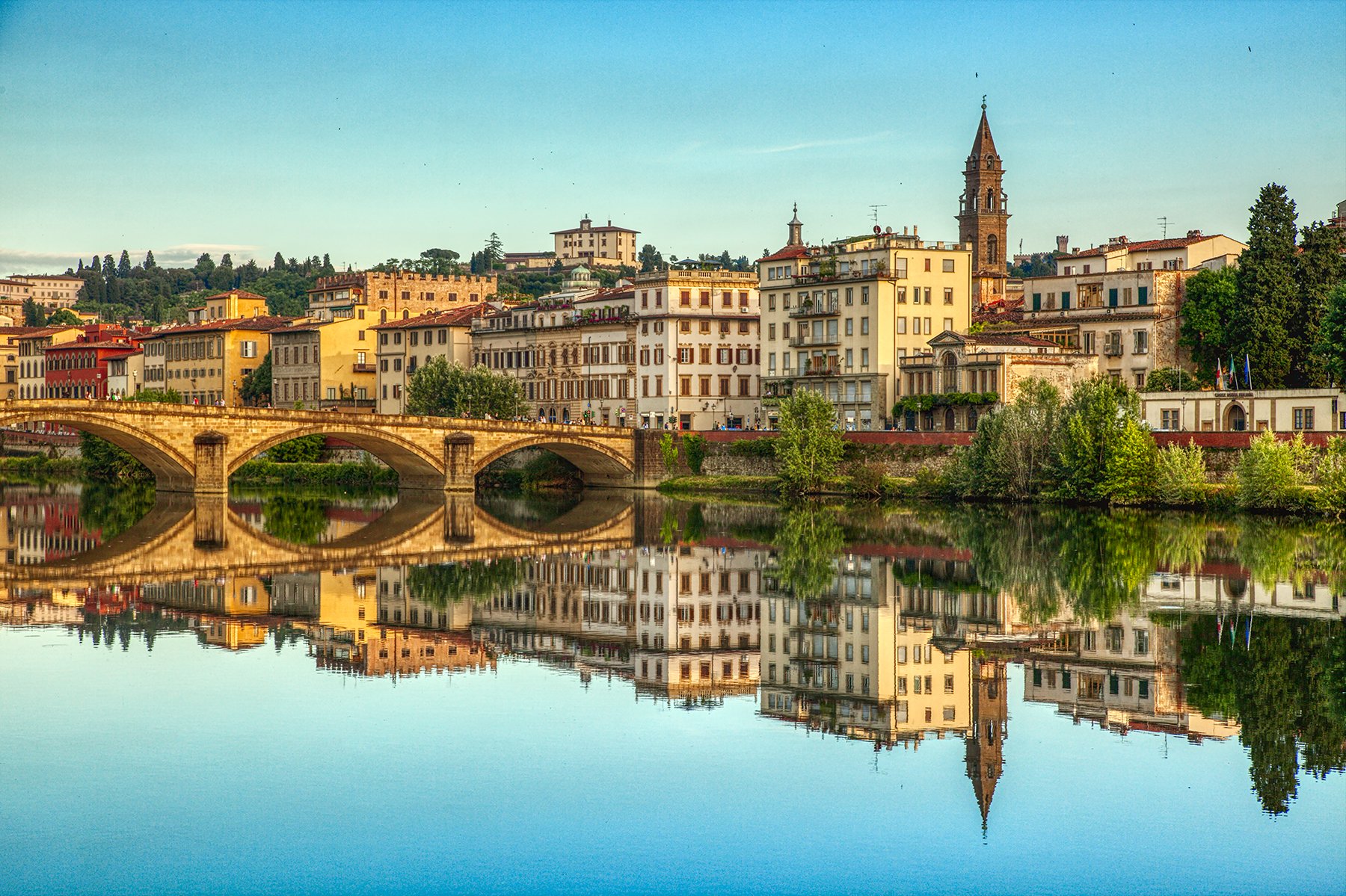 Florence city skyline reflecting in the Arno River with historic bridge and buildings in Italy.