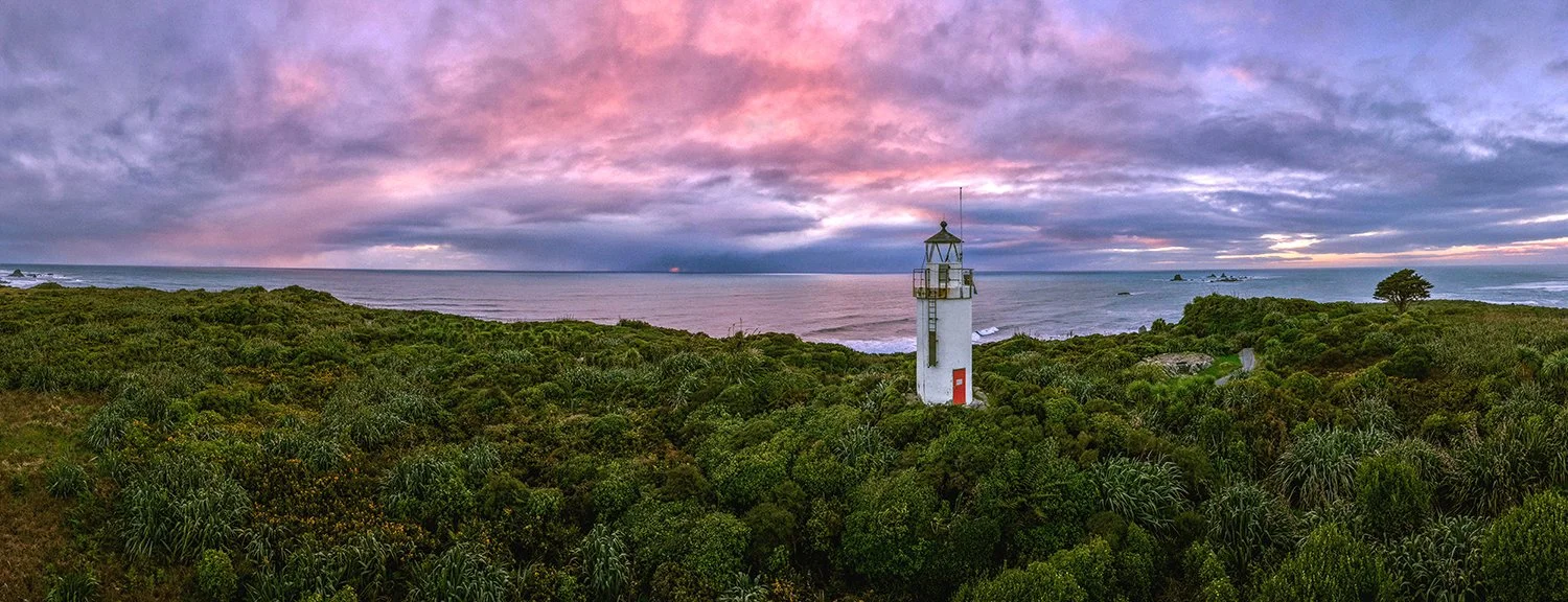 Panoramic view of a historic lighthouse surrounded by native bush at sunset.