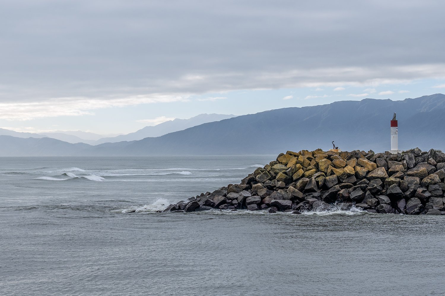 Beacon on a rocky breakwater with mountains beyond on New Zealand's West Coast.