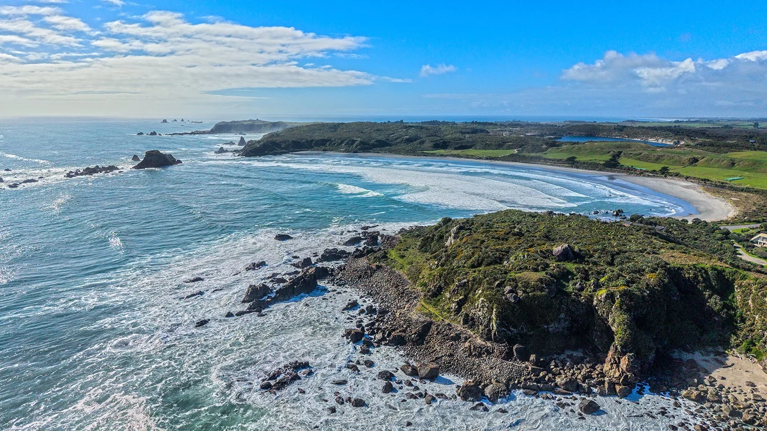 Waves rolling onto a West Coast beach with sea stacks offshore.