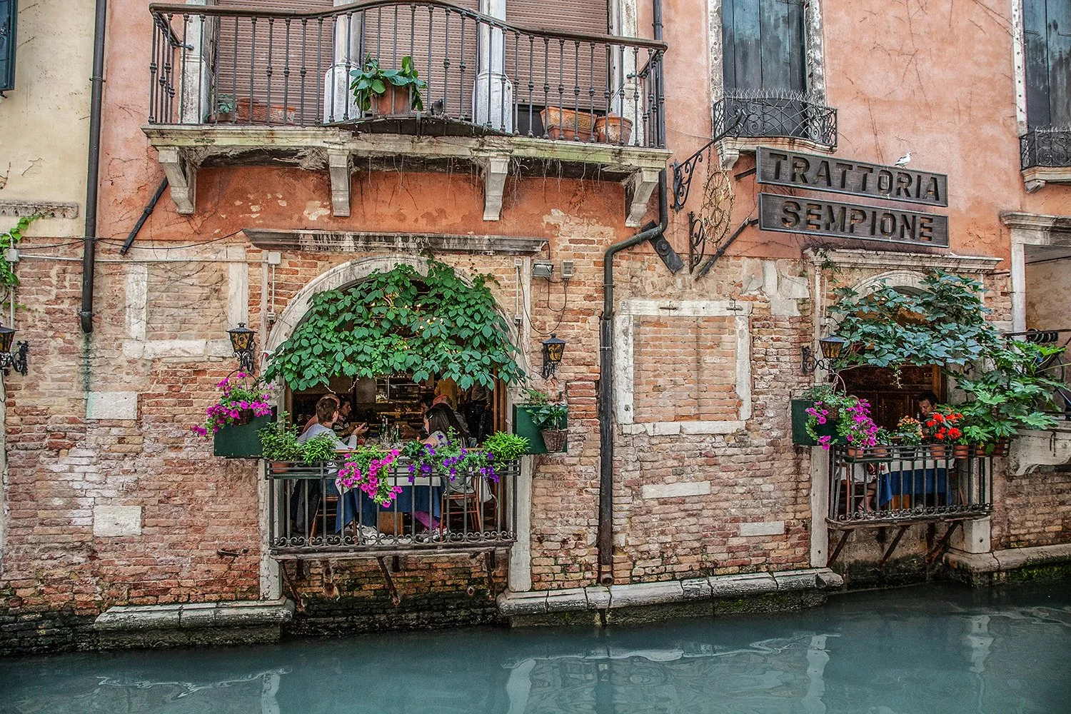 Italian restaurant beside a Venetian canal with flowers and balconies.