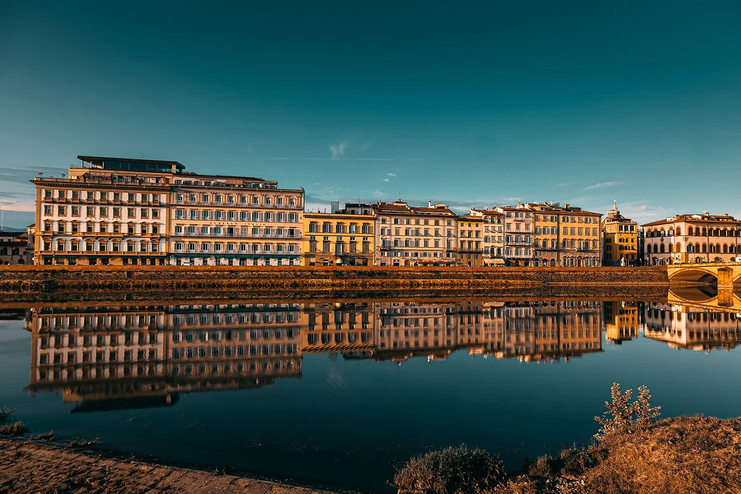 Florence buildings reflected in the Arno River at sunset.