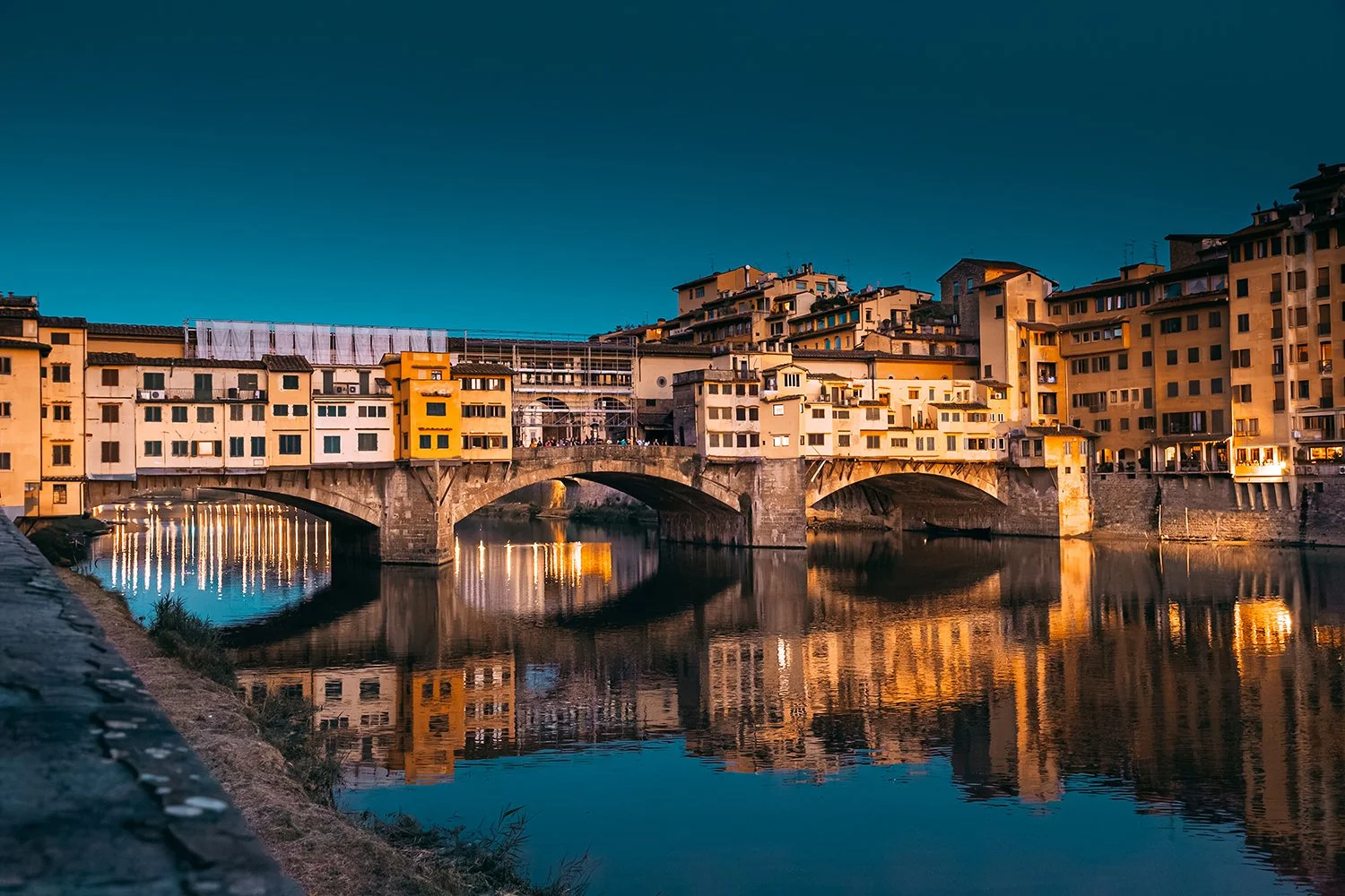 Ponte Vecchio bridge illuminated at dusk with reflections in the Arno River.