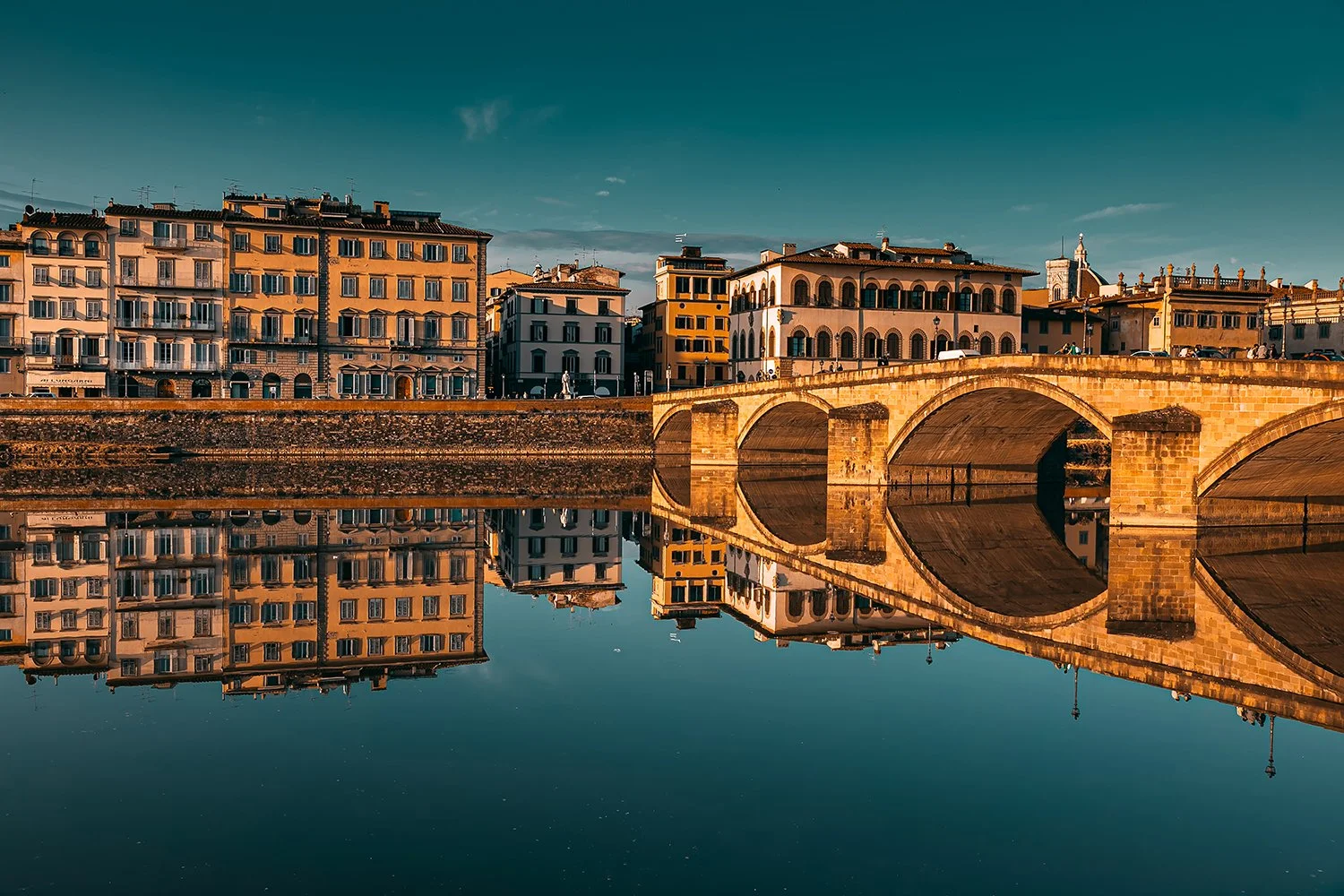 Florence bridge reflected in the Arno River at golden hour, Italy.