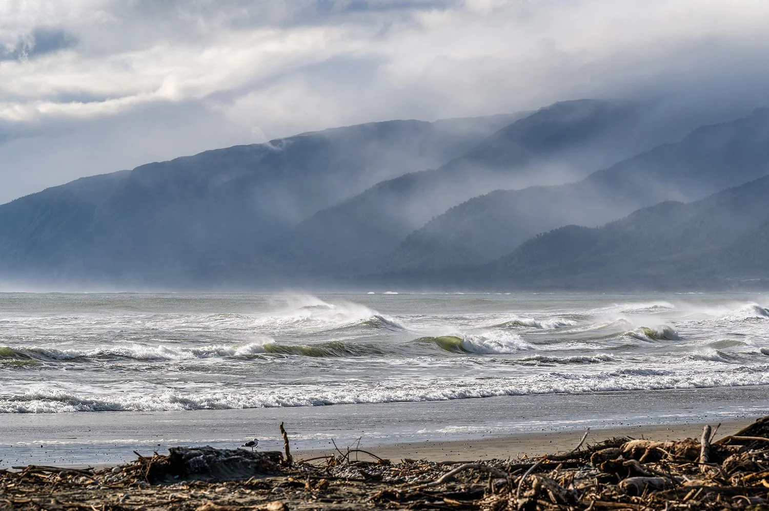 Sea spray blowing across waves beneath misty mountain ranges.