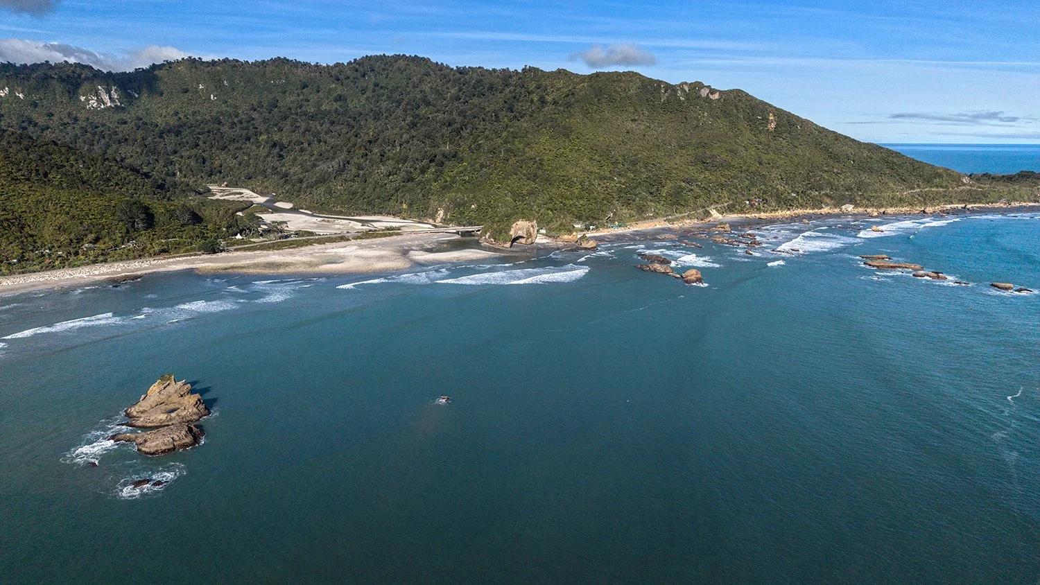 Aerial coastal landscape with offshore rock formation and rugged shoreline.