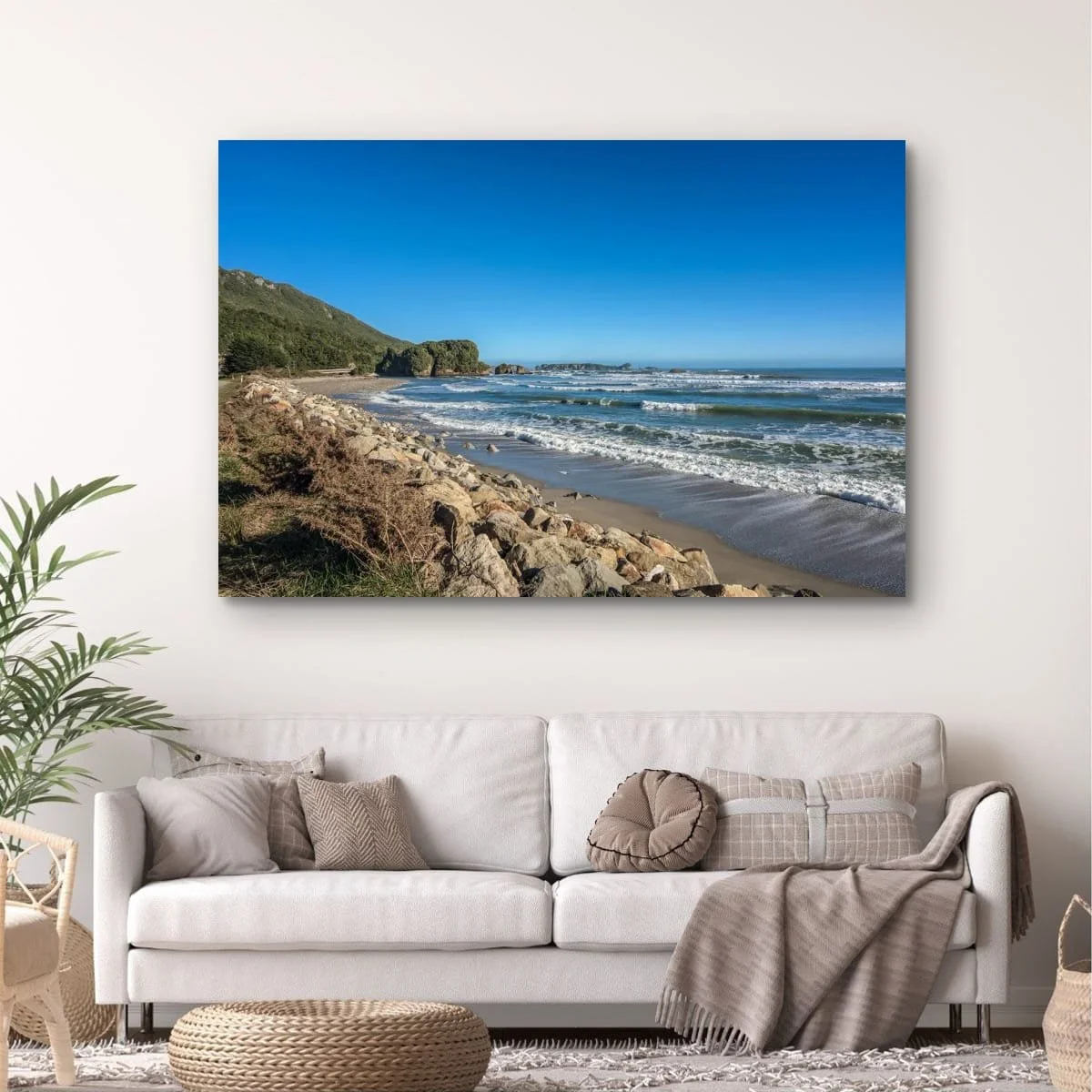 Waves rolling onto a rocky West Coast beach with distant sea stacks beneath a clear blue sky.