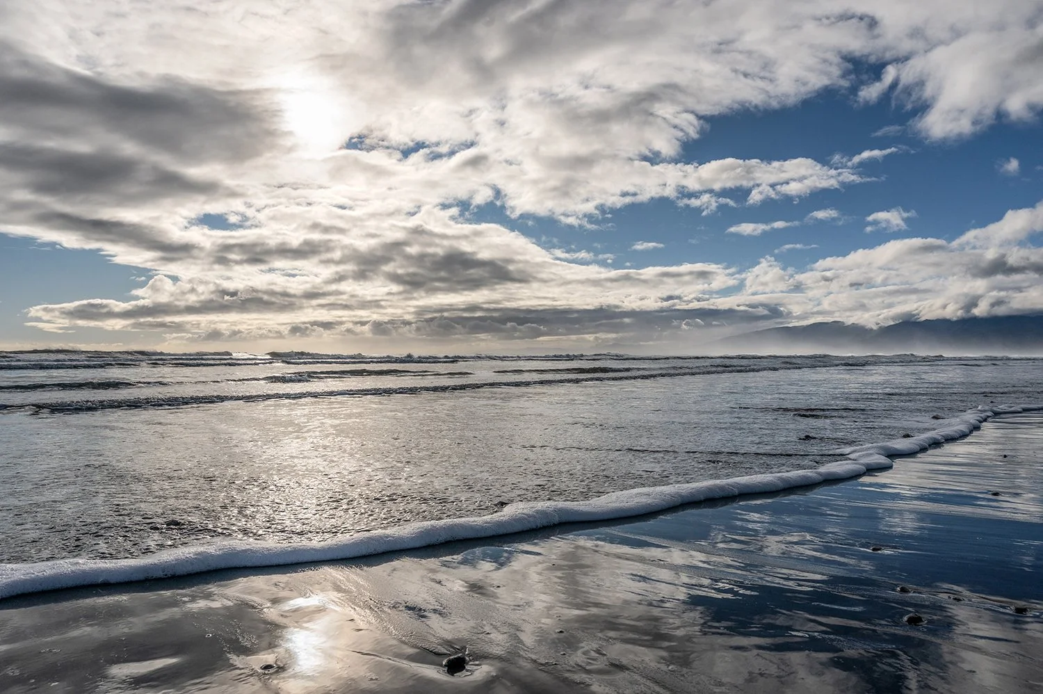 Dramatic clouds over mountains and breaking surf on the West Coast.