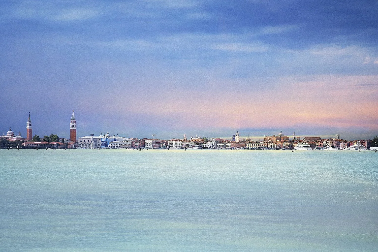 Panoramic view of Venice skyline across calm water beneath pastel skies.