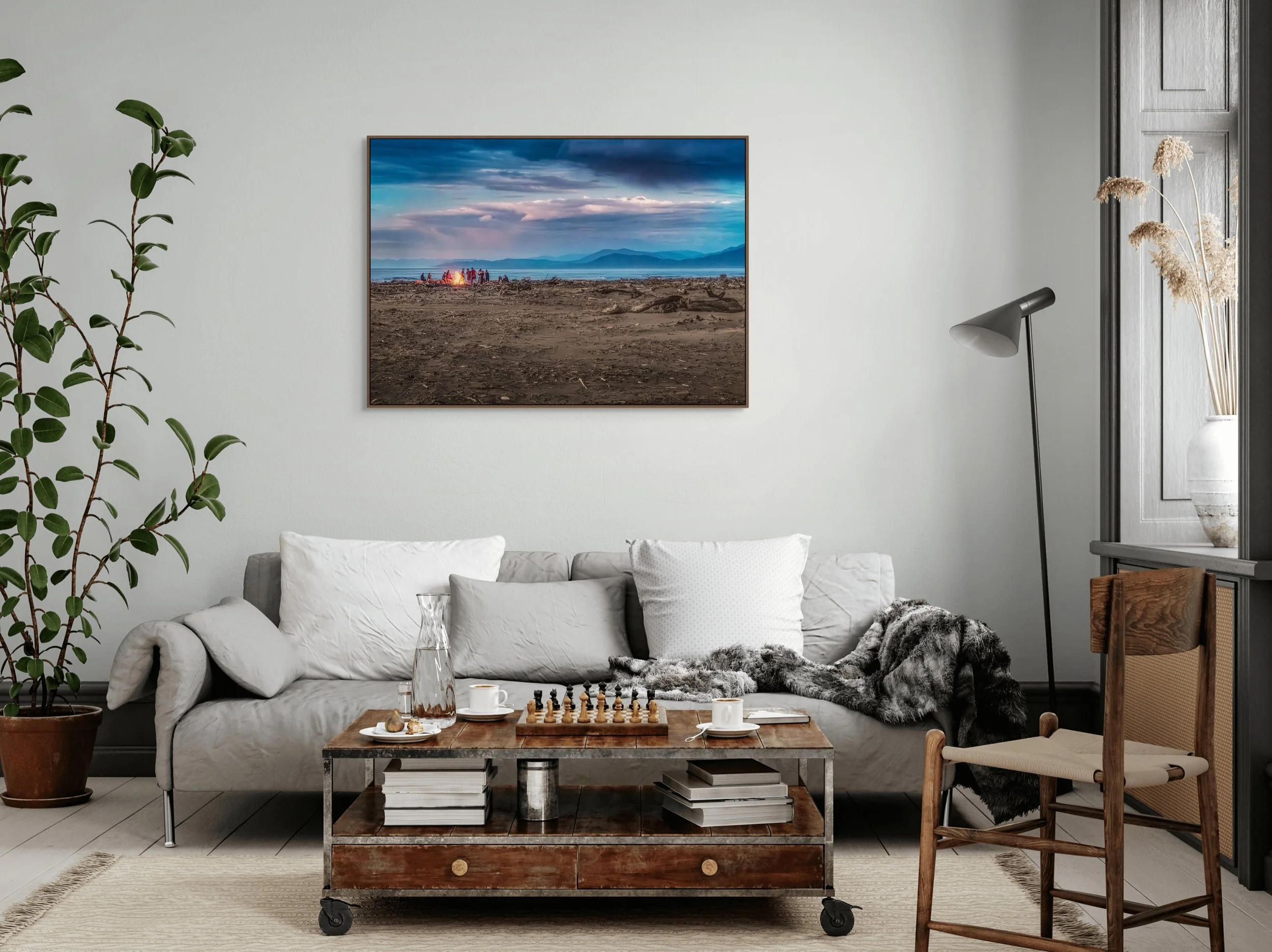 People gathered around a beach bonfire on a driftwood covered coastline at dusk.