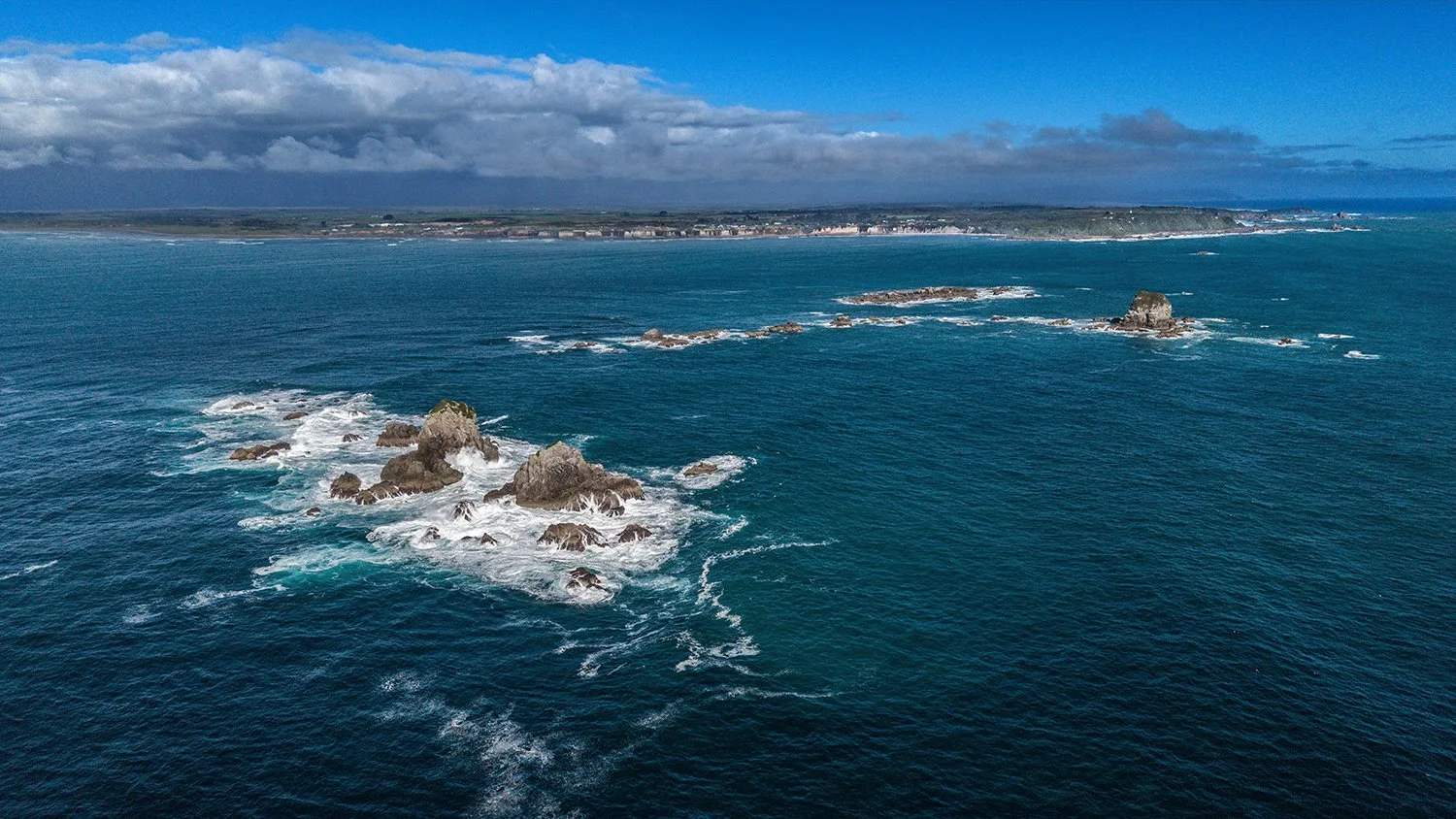 Aerial view of ocean currents moving around coastal rocks and reefs.