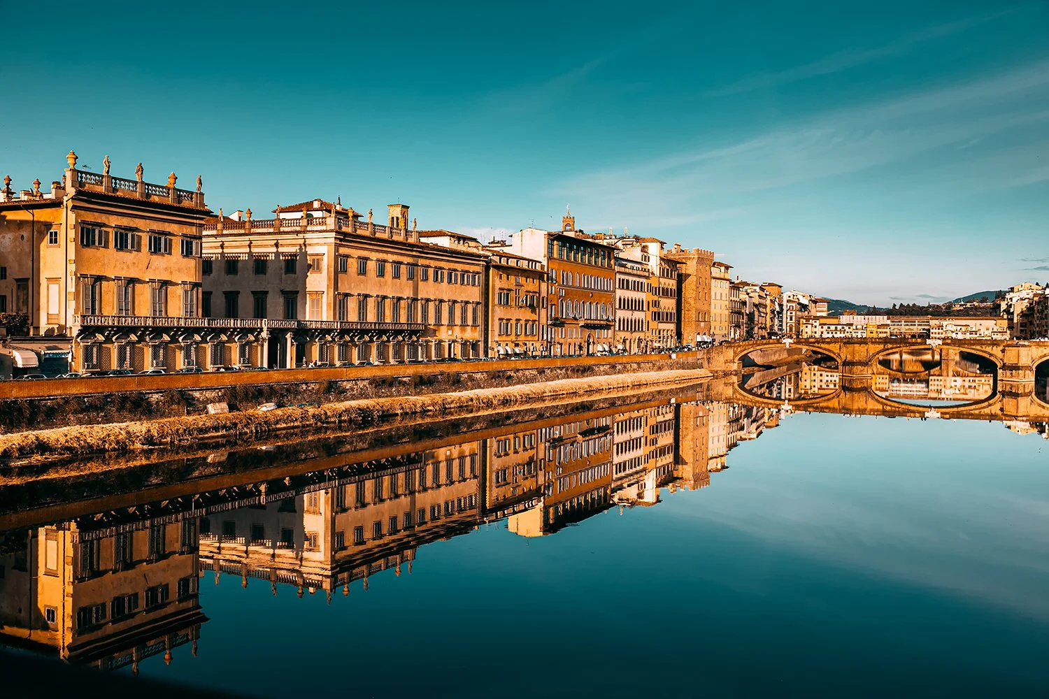 Historic Florence buildings reflected in the Arno River at sunset.