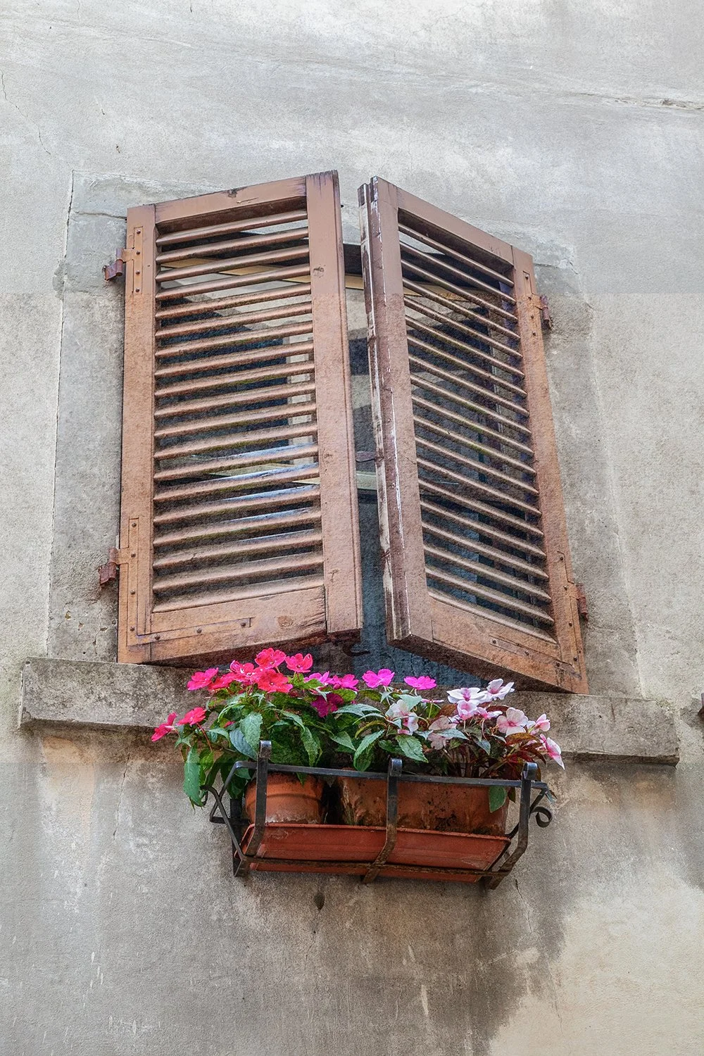 Rustic Italian window with wooden shutters and pink flowers in a window box.