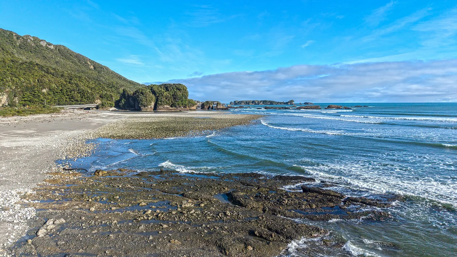 Coastal river mouth meeting the Tasman Sea beneath native forest-covered hills.