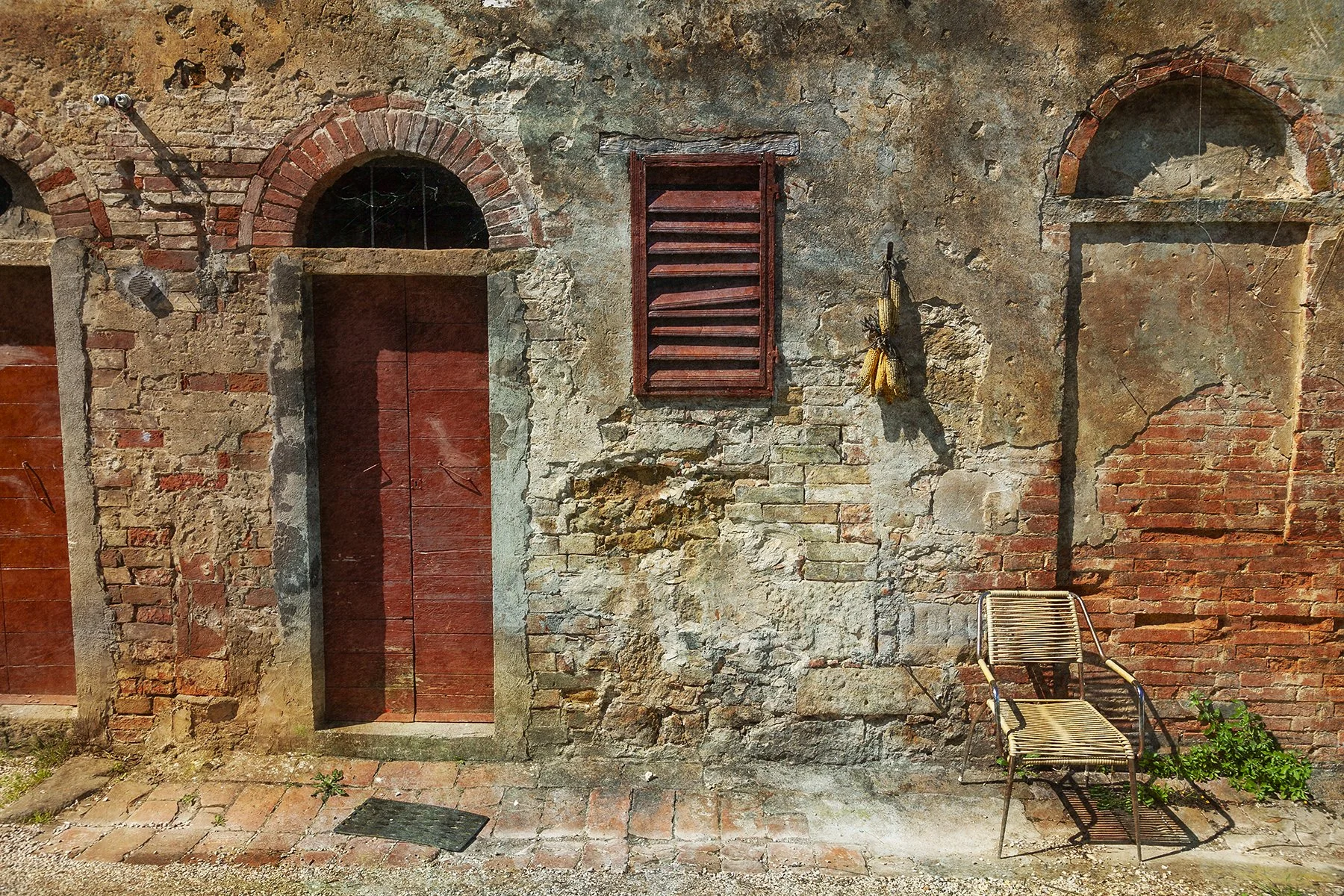 Italian travel fine art photograph of a lone chair rests quietly against an aged brick wall, where sun-faded shutters, worn plaster and weathered doors speak, by From The Field.
