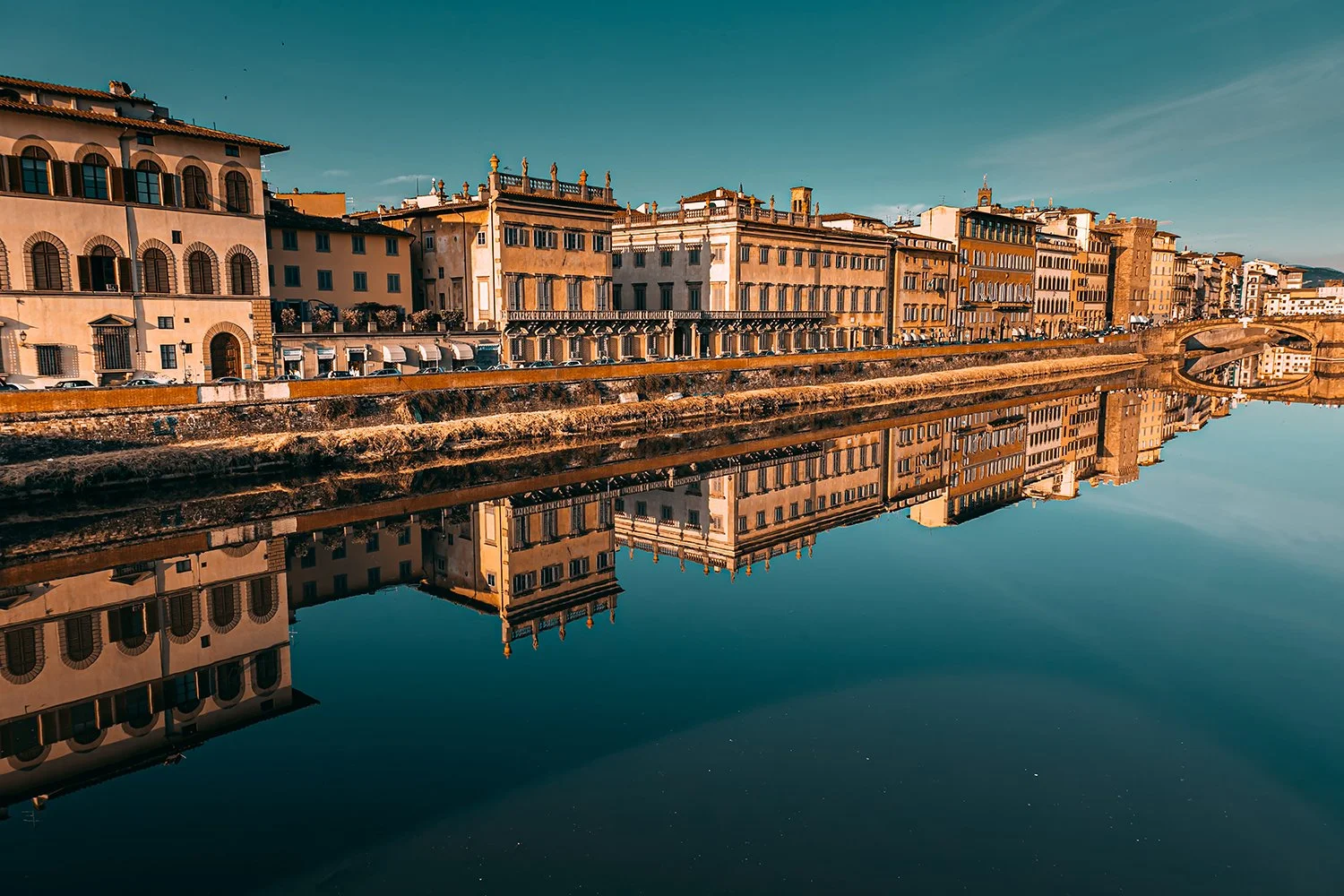 Florence cityscape with river reflections under warm evening light.