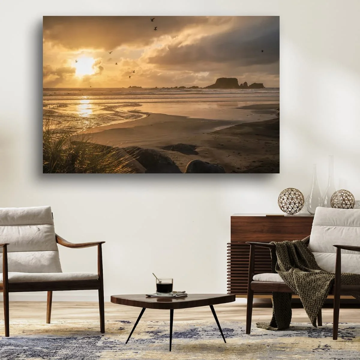 Seabirds flying across a golden sunset above wet sand, ocean waves and distant coastal rock formations.
