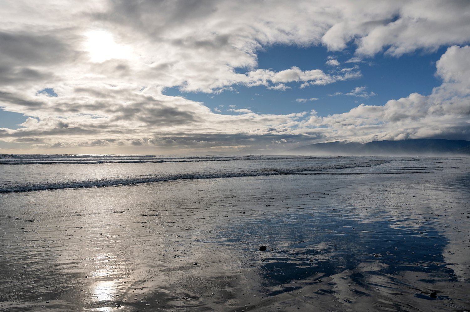 Sunlight reflecting across wet sand after the tide on the West Coast of New Zealand.