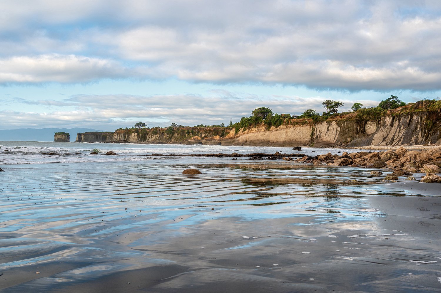 Long reflective shoreline beneath coastal cliffs on the West Coast.