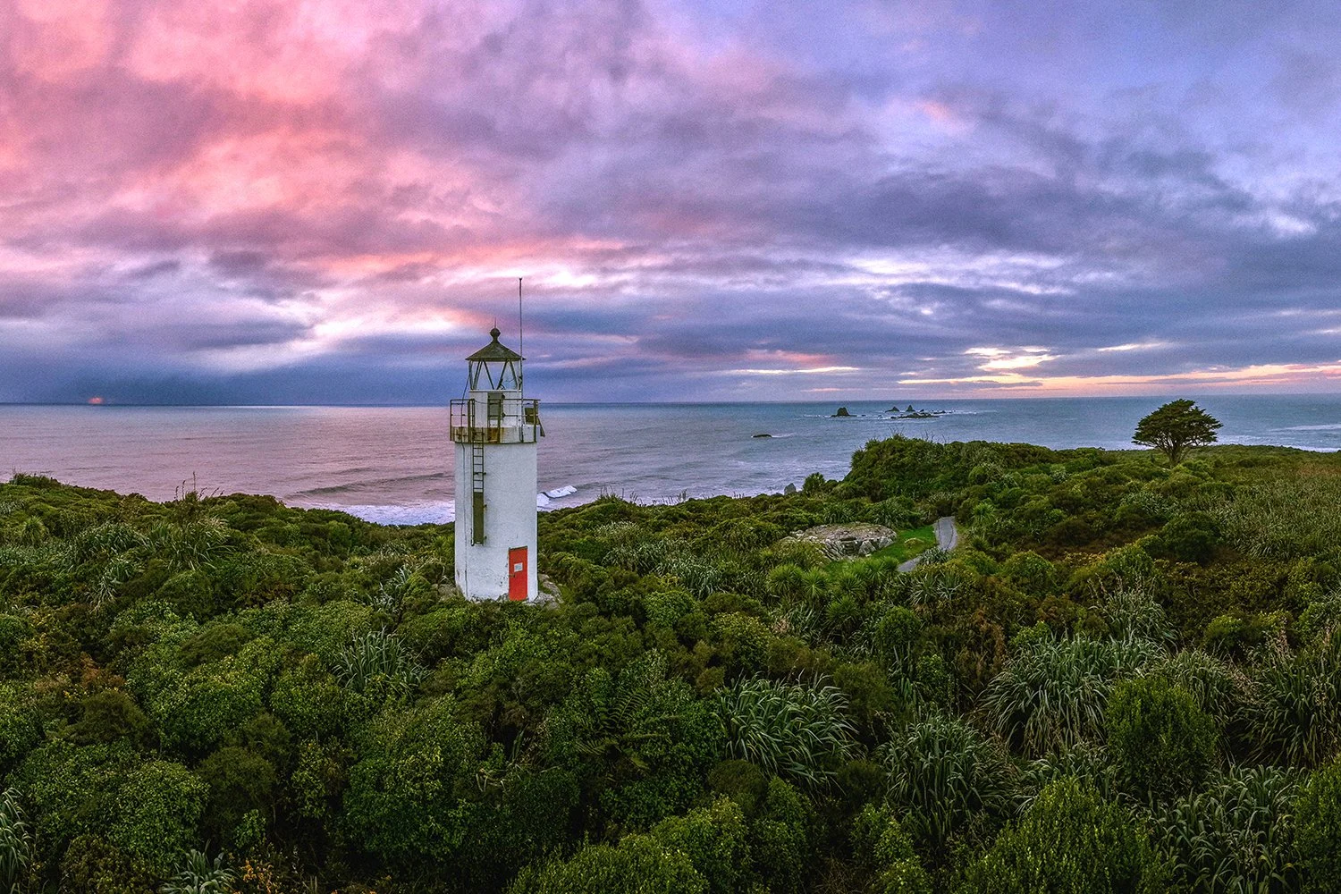 Panoramic view of a historic lighthouse surrounded by native bush at sunset.