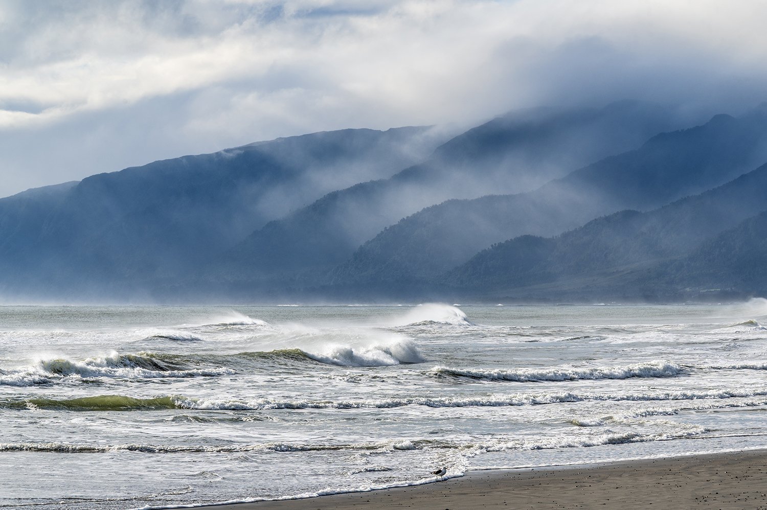 Waves breaking beneath mist-covered mountain ranges on the West Coast of New Zealand.