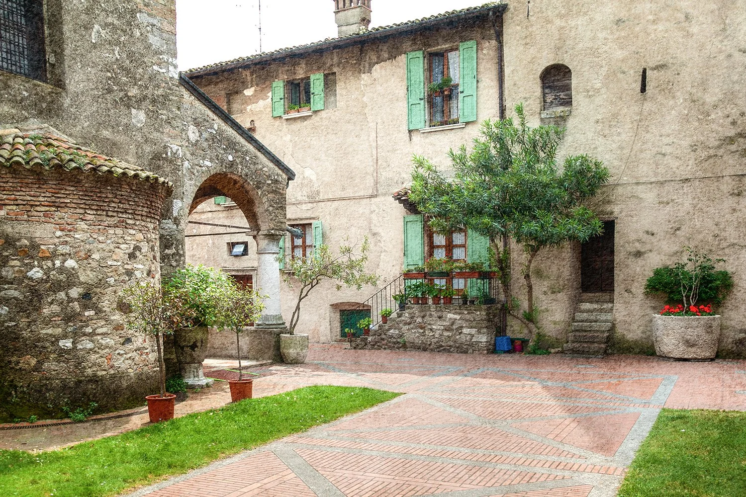 Quiet Tuscan courtyard with stone walls, potted plants and historic architecture.