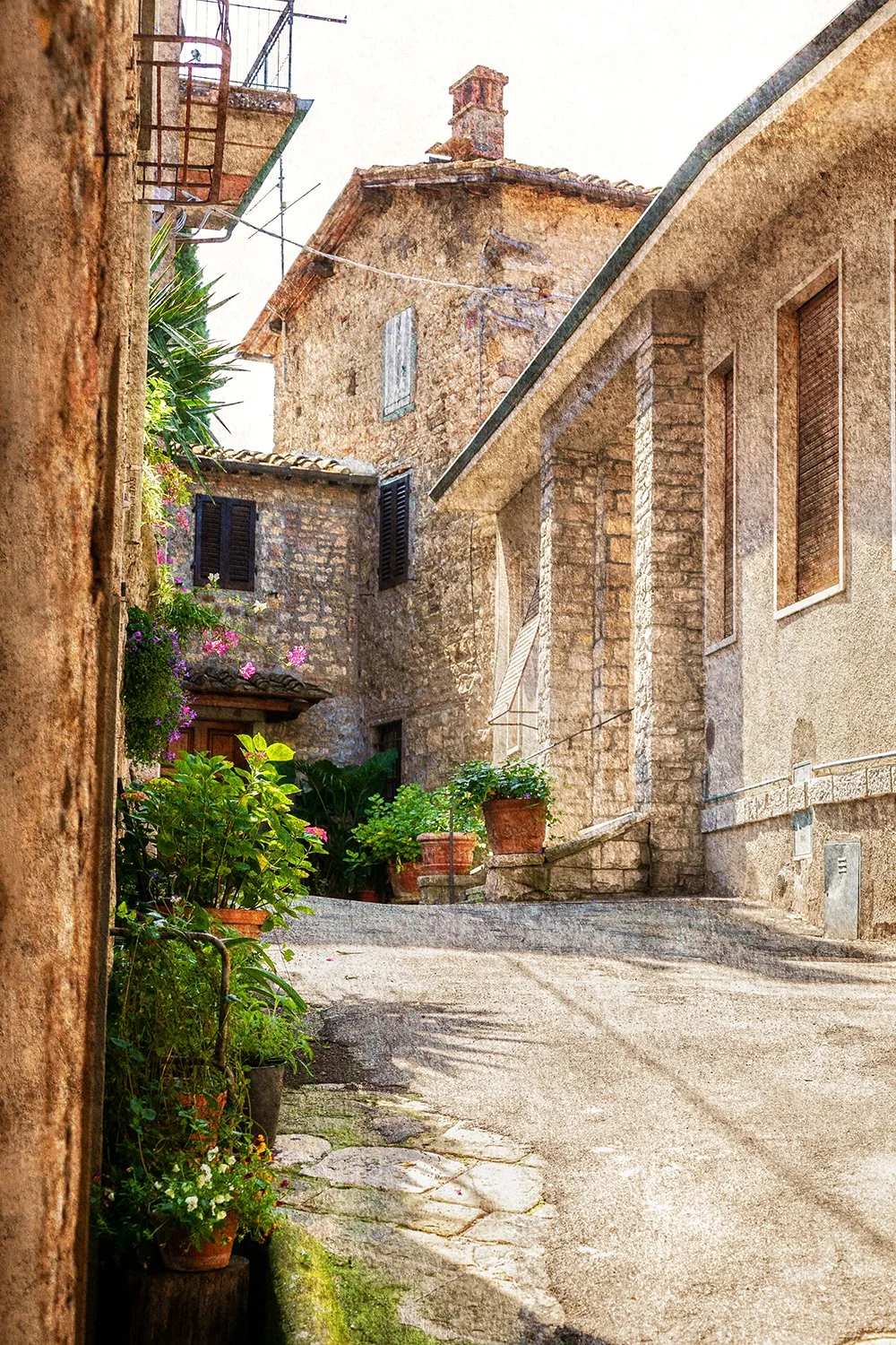 Narrow Tuscan laneway lined with flowers, stone walls and historic buildings.