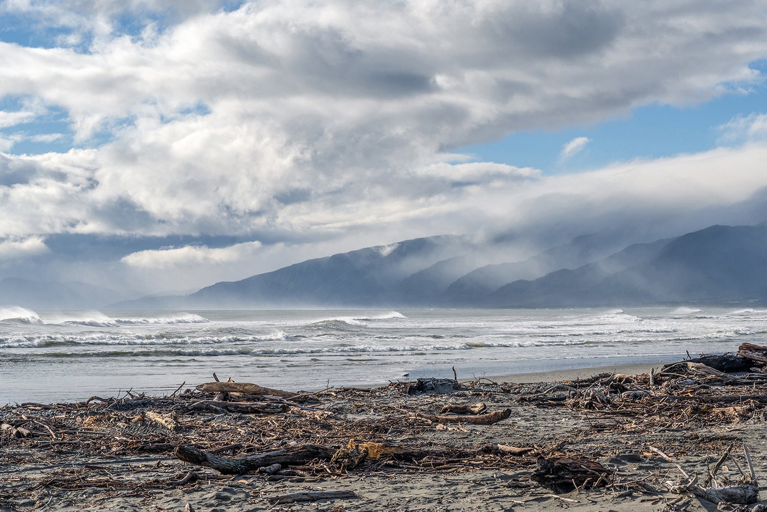 Mist-covered mountains above surf on the West Coast.