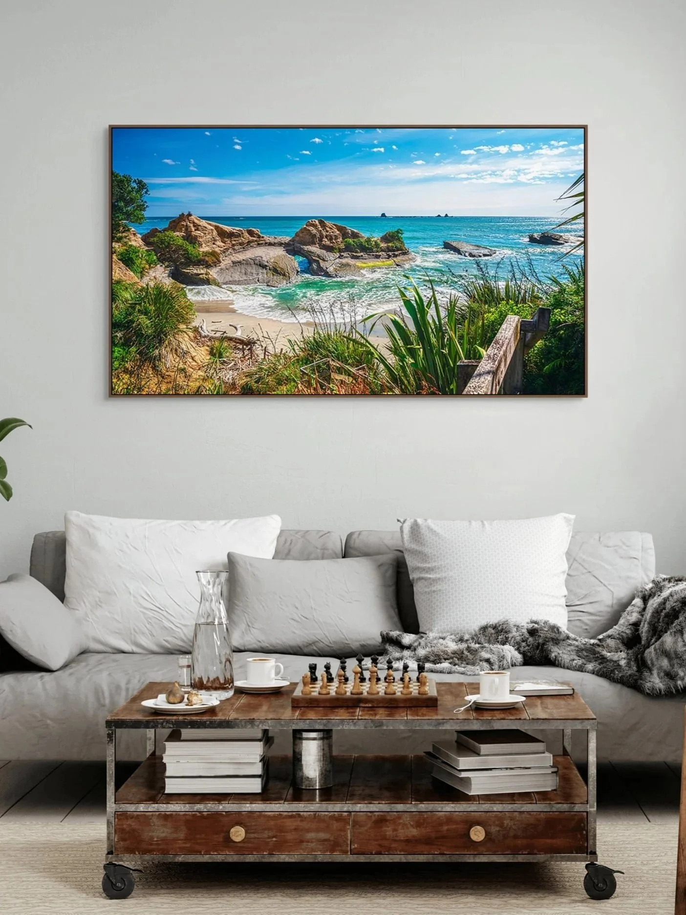 Living room with white sofa, wooden coffee table, gray rug, contemporary decor, large wall art of a beach scene with rocks and ocean, and a chess set.