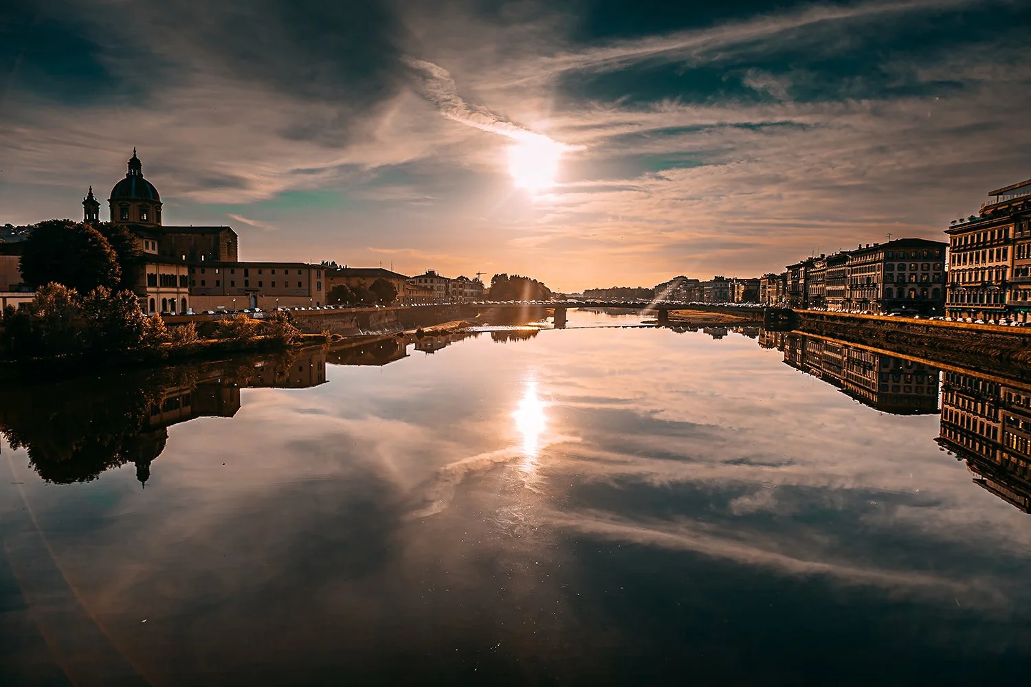 Florence skyline reflected in the Arno River beneath a glowing Tuscan sky.
