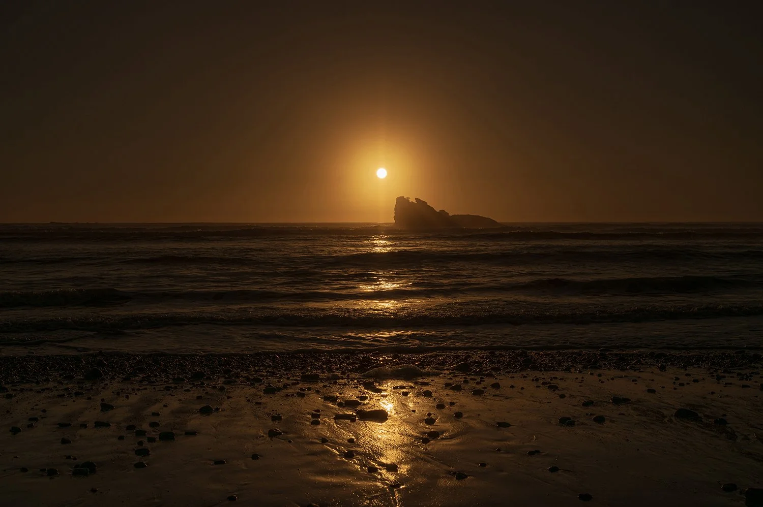 Golden sunset above offshore rock reflecting across the Tasman Sea.