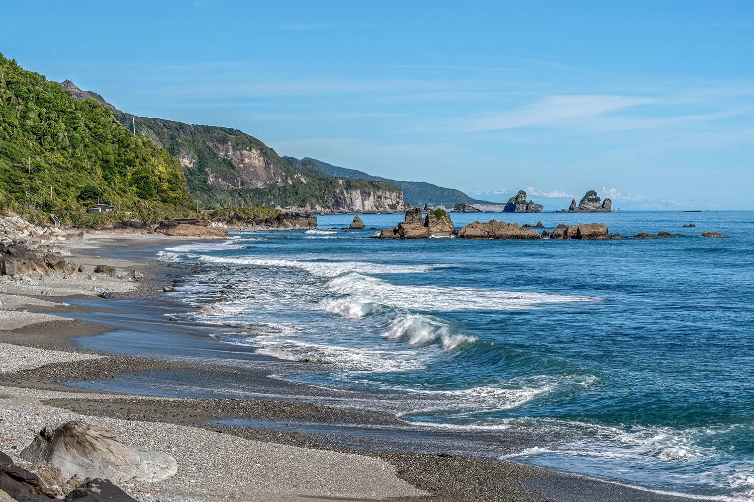 West Coast shoreline with waves, sea stacks and distant mountains.