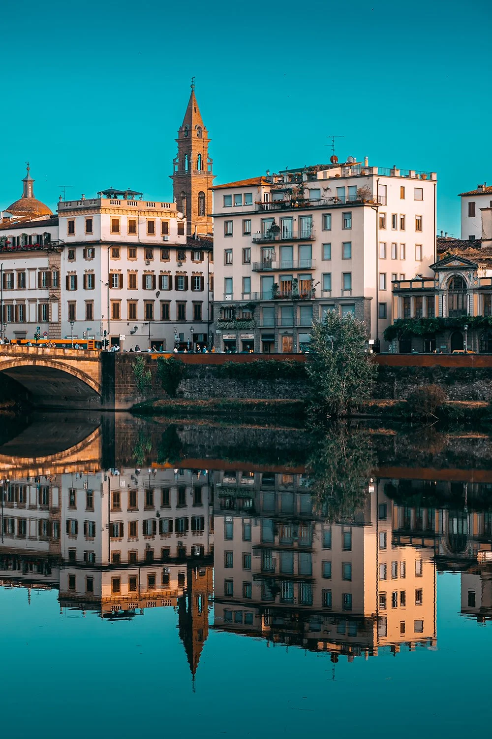 Tuscan buildings and church reflected in calm water.