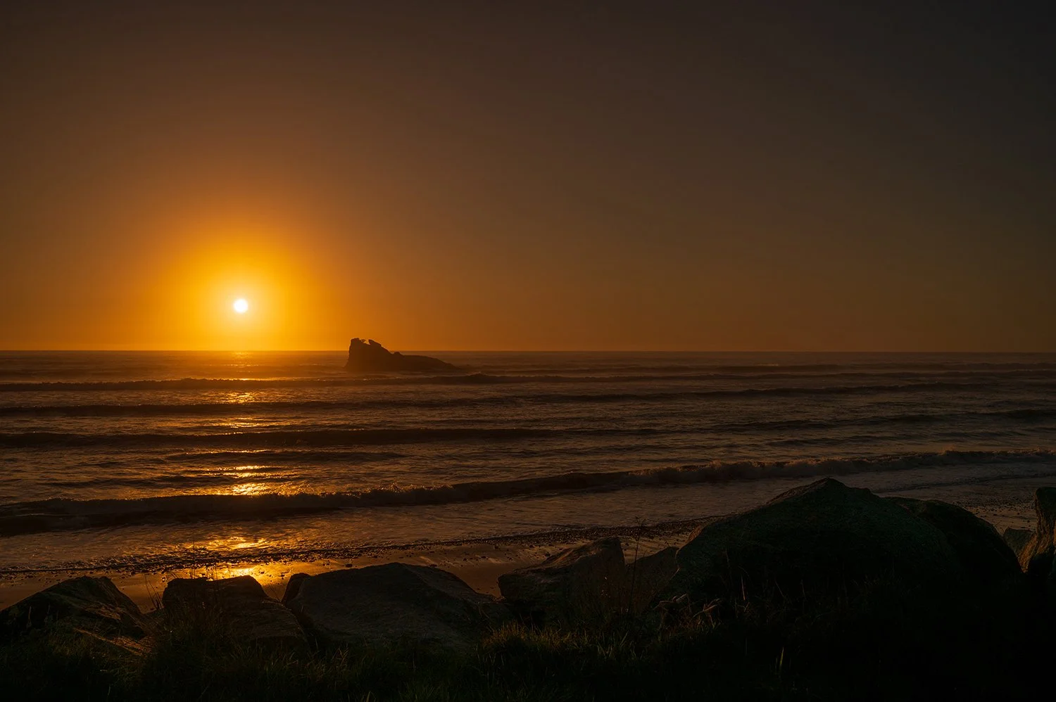 Golden sunset reflecting across the Tasman Sea with offshore rock formation.
