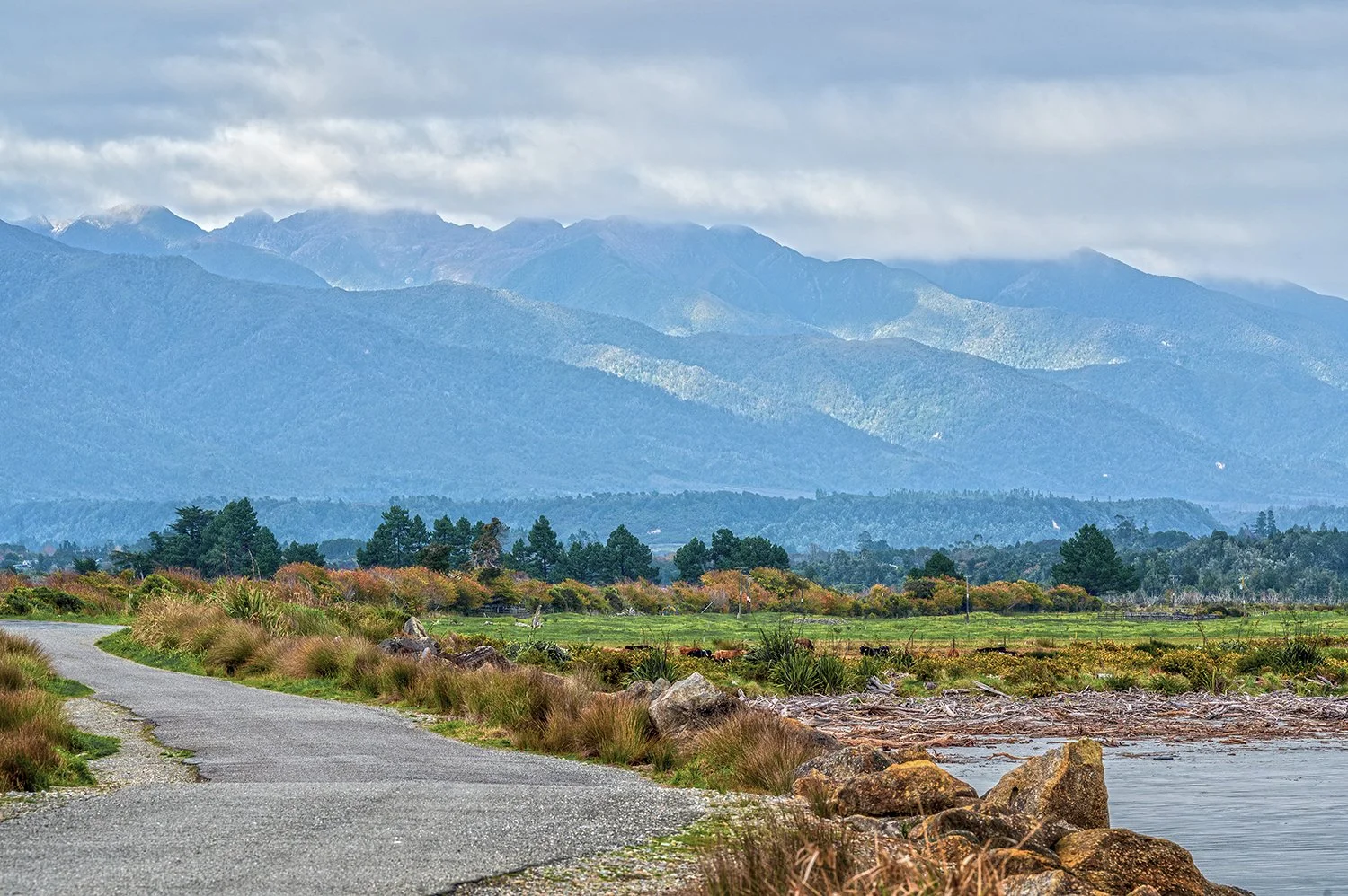 Country road leading towards layered mountain ranges on the West Coast.