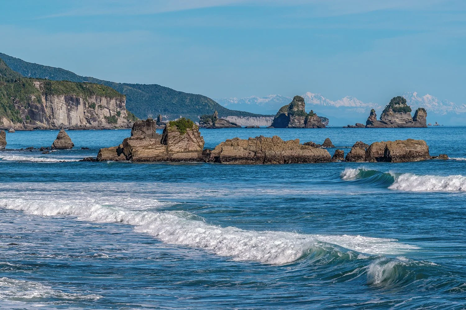 Coastal rocks, ocean and distant snow-capped mountains.