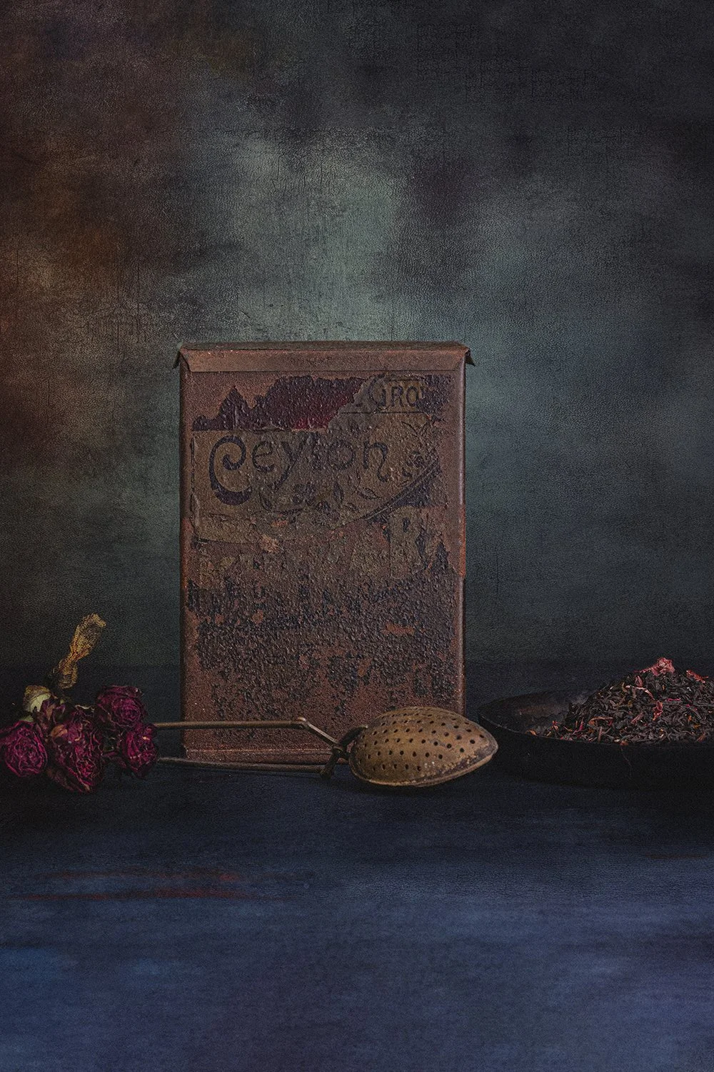 Vintage tea tin with dried roses and tea accessories.