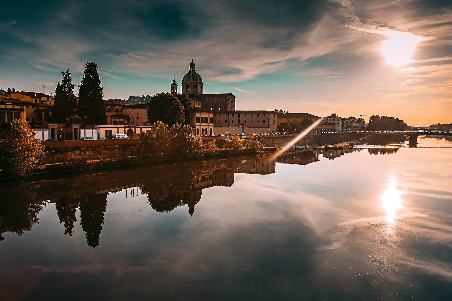 Florence skyline reflected in the Arno River during golden hour.