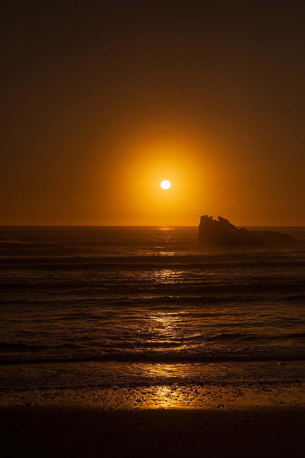 Warm orange sunset over the Tasman Sea with silhouetted sea stack and gentle waves.