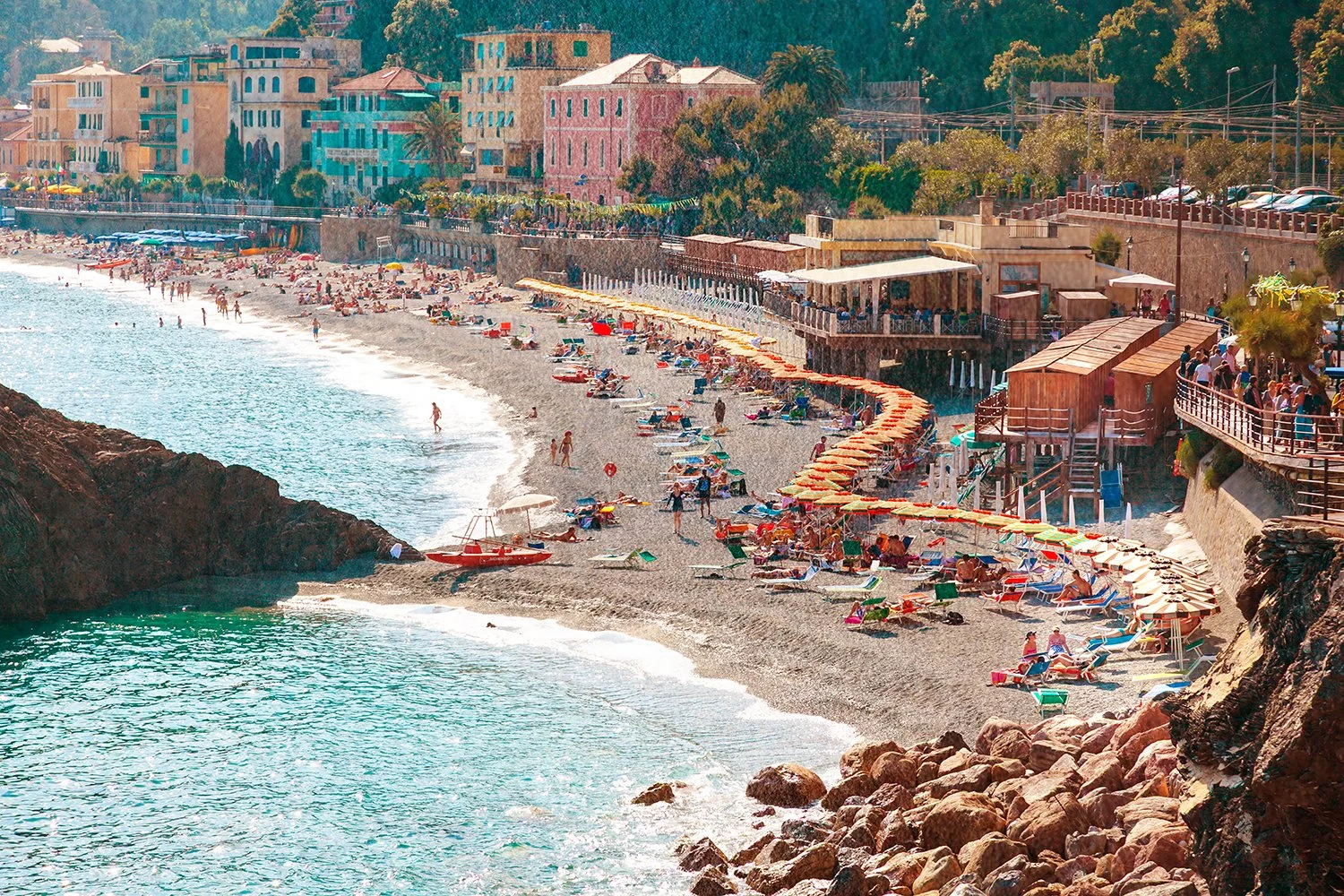 Busy Mediterranean beach with colourful umbrellas and turquoise water.